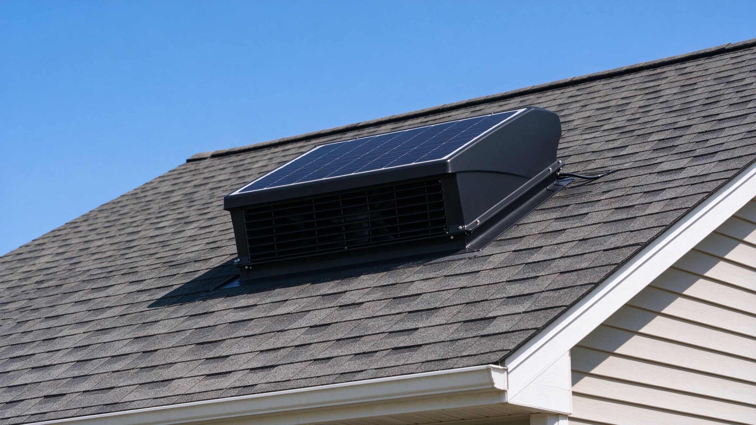 A black solar powered attic ventilation fan mounted on a residential asphalt shingle roof on a sunny day